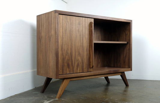 Front view of the hand-built walnut cabinet featuring a single sliding door and two adjustable shelves in a mid-century modern design